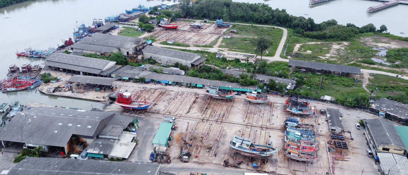 ภาพมุมสูงของคานเรือ ท่าเทียบเรือ และโรงงานของบริษัทริมแม่น้ำปัตตานี